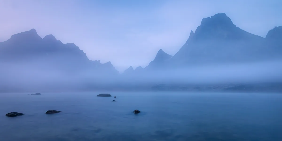 Gezackte Gipfel über dem See im blauen Nebel – Grönland