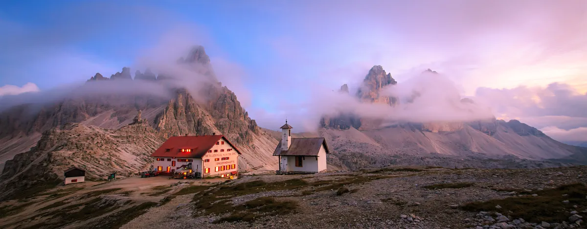 Hütte und Kapelle vor wolkenverhangenen Gipfeln – Südtirol