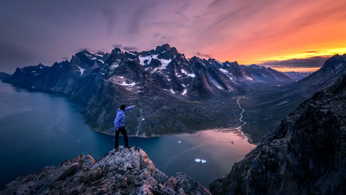 Person auf einem Felsen über dem Fjord bei Sonnenuntergang – Grönland