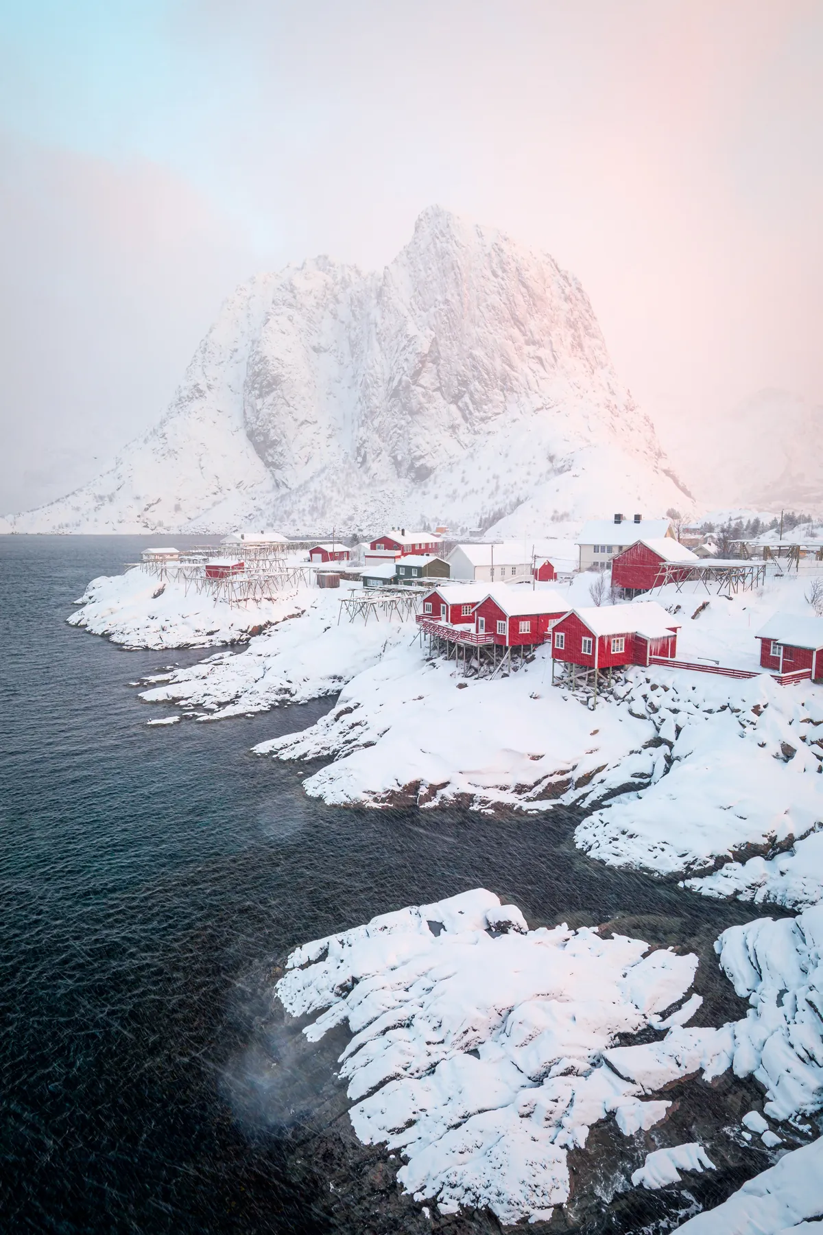 Rote Fischerhütten im Schnee vor verschneiten Gipfeln – Lofoten, Norwegen