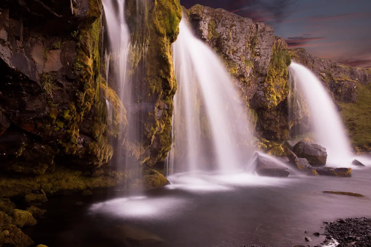 Kaskaden des Kirkjufellsfoss über bemoosten Fels in der Dämmerung – Snæfellsnes, Island