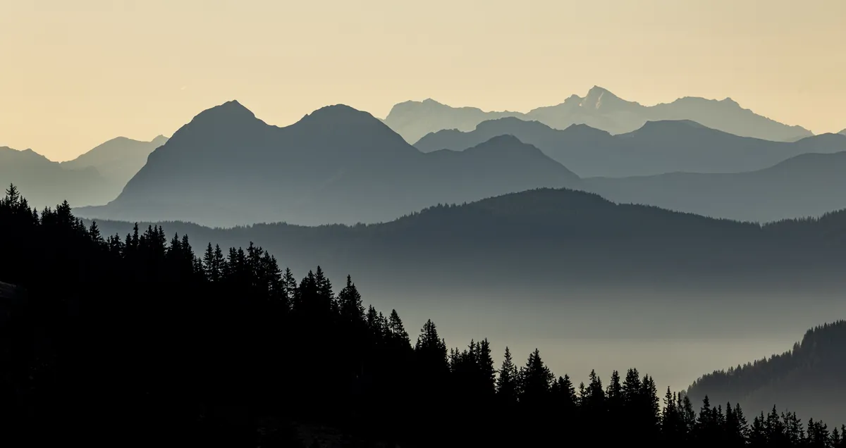 Gestaffelte Berge im Dunst über dunklem Wald – Saalbach, Österreich